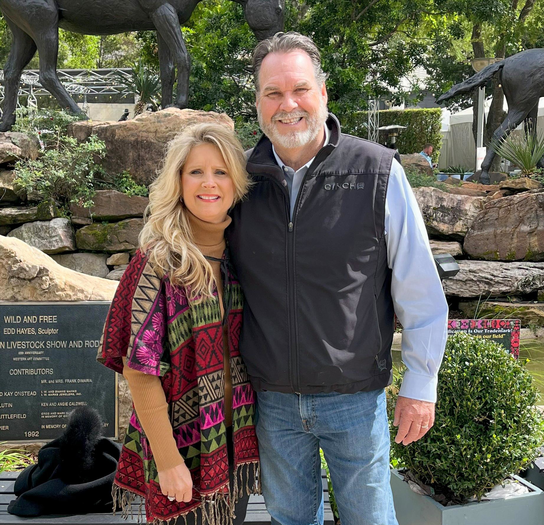 Smiling couple posing outdoors near sculptures.